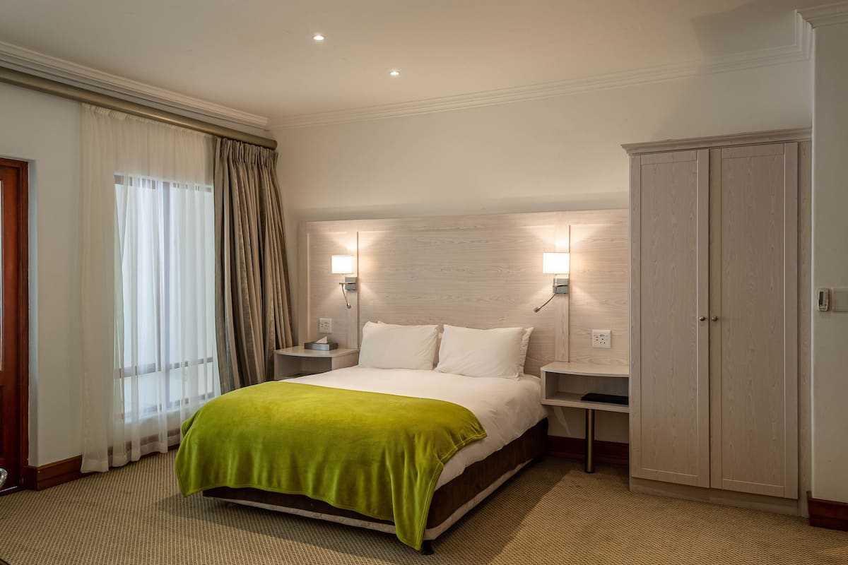 Een hotelkamer met een bed, nachtkastjes, een kledingkast en een raam met gordijnen.
