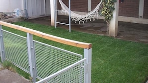 A fenced outdoor area with a hammock, a grassy lawn, and a building with a brick exterior. - Neuquen Hostel Portal de Sueños (Neuquen)