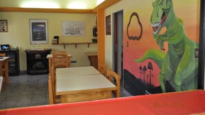A dining area with a table and chairs, a fireplace, and a mural of a dinosaur. - Neuquen Hostel Portal de Sueños (Neuquen)