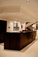 Un área de recepción moderna con un mostrador de madera oscura, iluminación empotrada en el techo y una escalera al fondo.