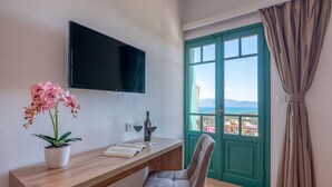 A room with a wooden desk, a potted orchid, a flat-screen TV, and a view through a green door. - Kaliviani Traditional Hotel (Kissamos)