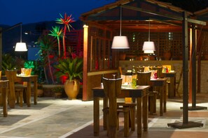 Un espace de restauration en plein air avec des tables et des chaises en bois, un coin salon abrité et des plantes décoratives.