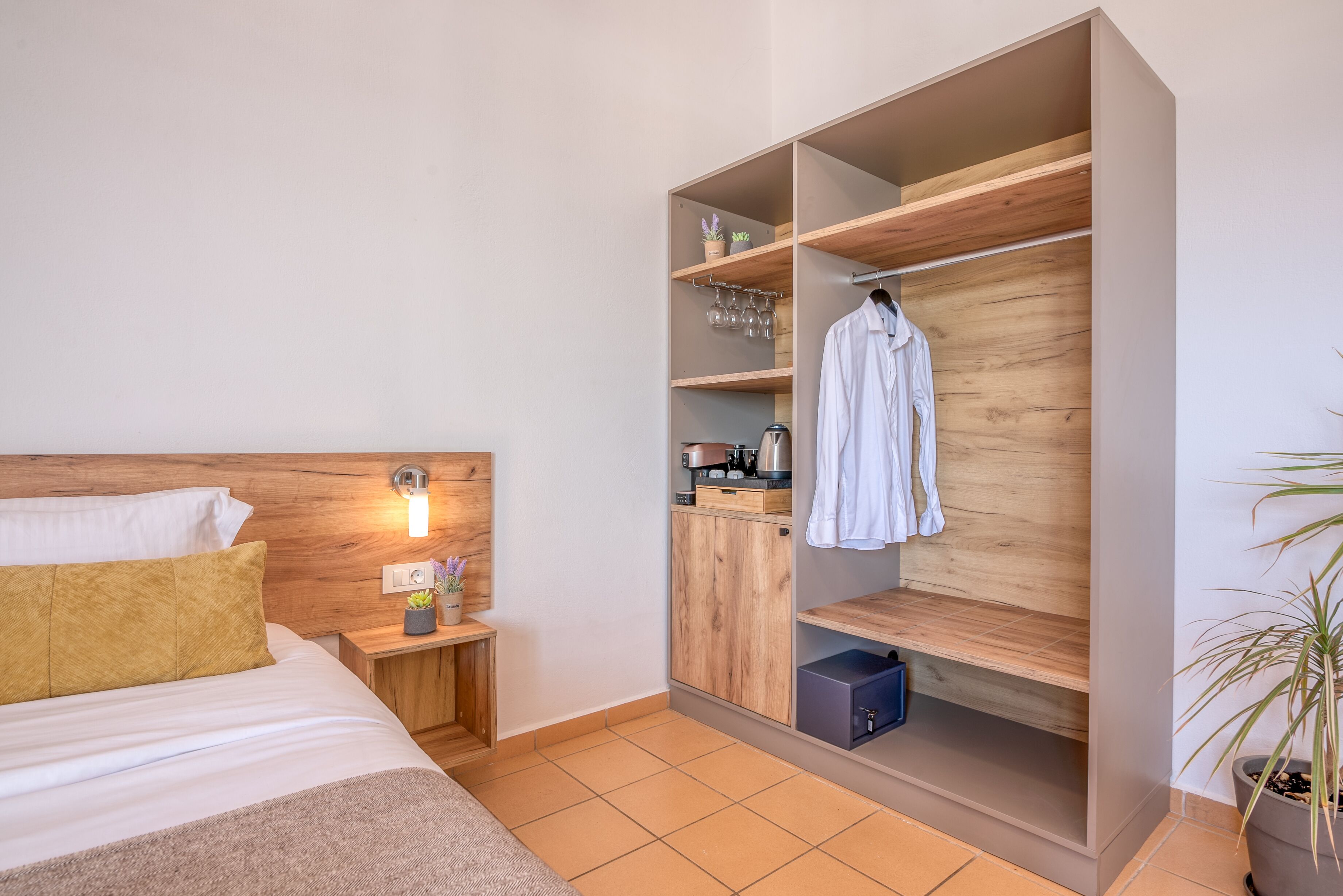 Una habitación de hotel con cama, mesita de noche, armario y una planta en maceta.