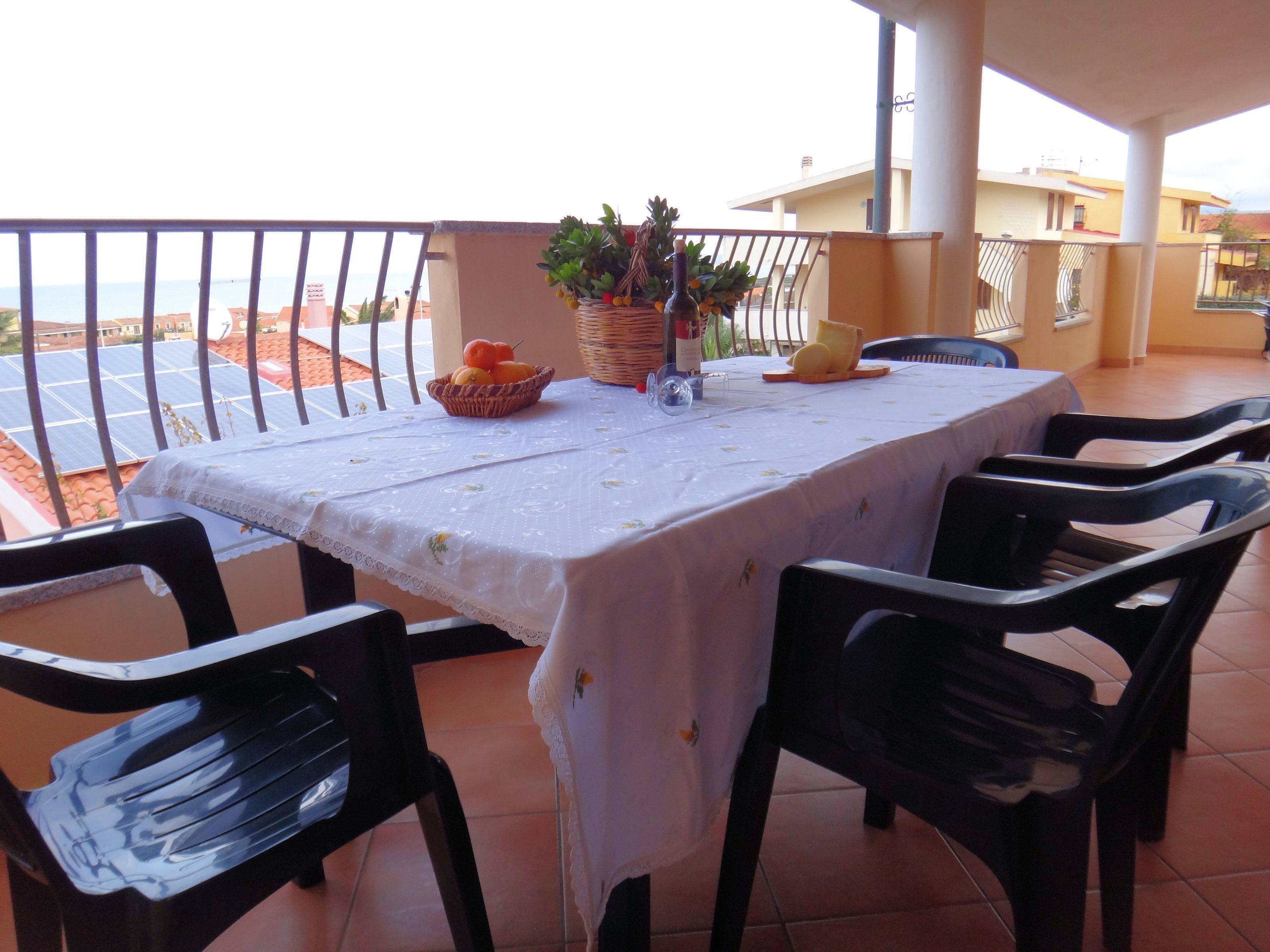 Een balkon met een eettafel, stoelen, een bloempot en uitzicht op de zee.