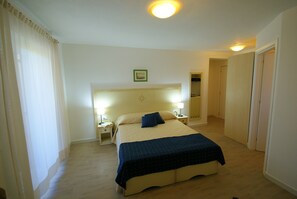 A hotel room with a large bed, bedside lamps, a nightstand, a framed picture on the wall, and a door leading to another room. - Sa Fiorida Apartments (Valledoria)