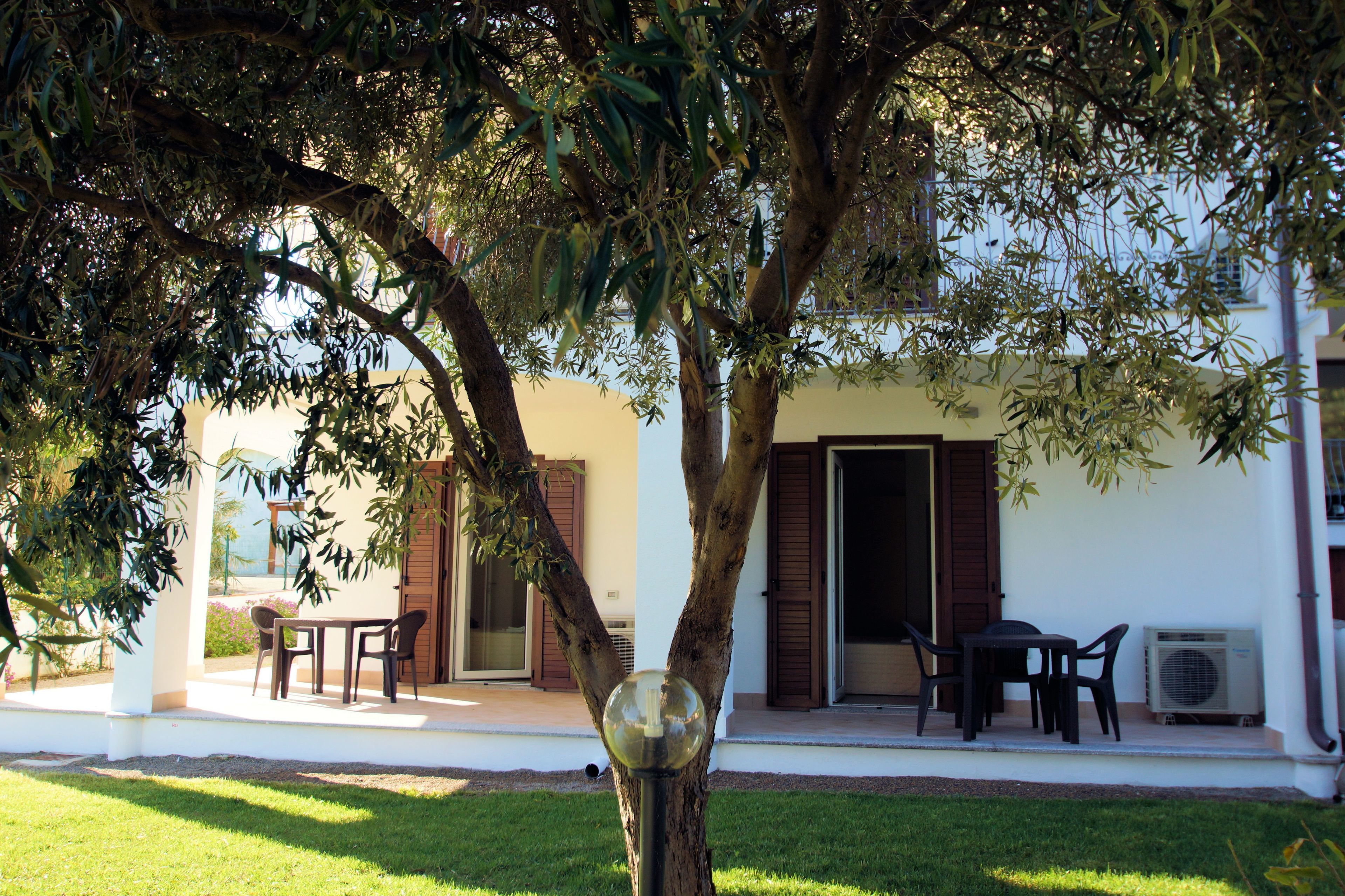 A patio with a table and chairs, a tree, and an air conditioning unit.