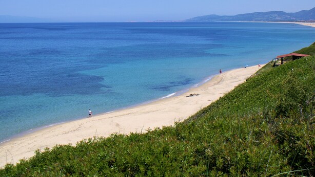 A beach with clear blue water, a sandy shore, and a small structure on the right. - Sa Fiorida Apartments (Valledoria)