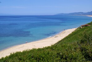 A beach with clear blue water, a sandy shore, and a small structure on the right. - Sa Fiorida Apartments (Valledoria)
