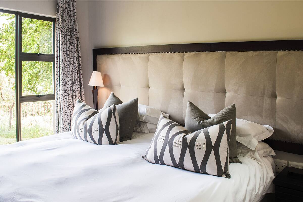 A hotel room with a large bed, two bedside lamps, and a window with curtains.
