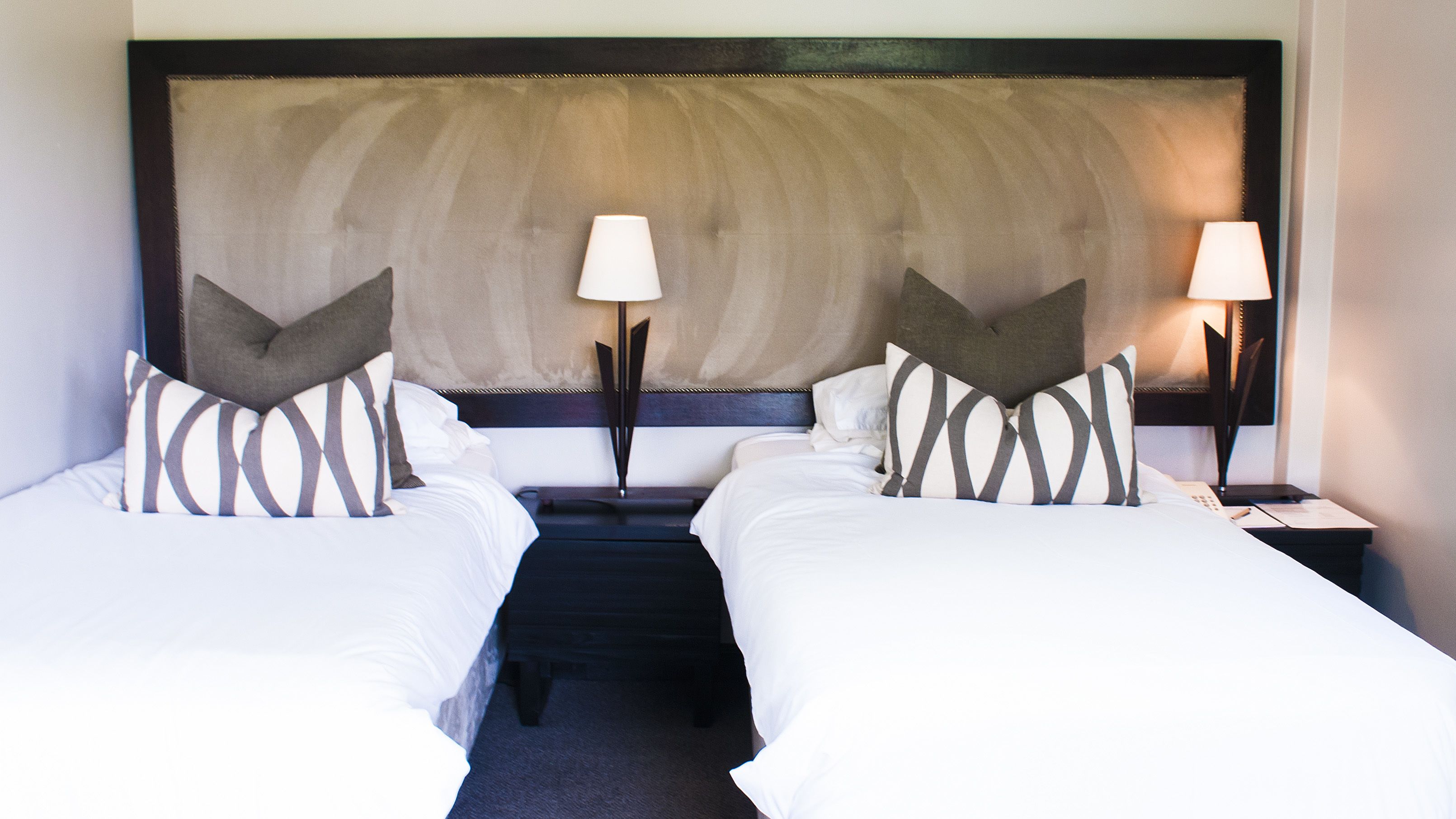 Une chambre d’hôtel avec deux lits simples, chacun étant équipé d’un oreiller et d’une table de chevet avec une lampe.