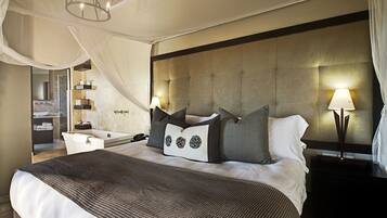 A spacious bedroom with a large bed, a nightstand, a bedside table, and a bathroom visible through an open door.