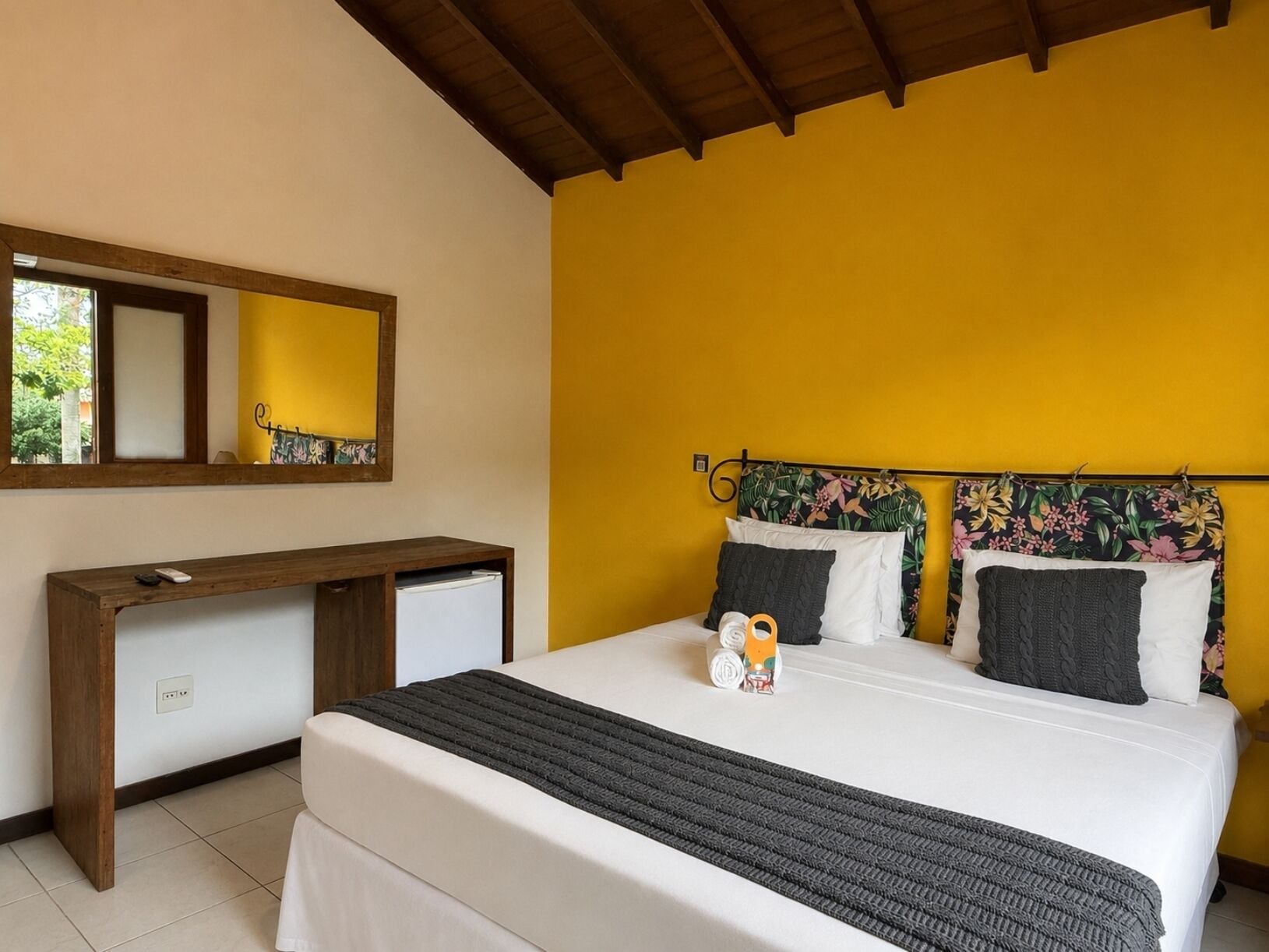 Un dormitorio con una cama, una mesita de noche, un espejo y una pared amarilla.