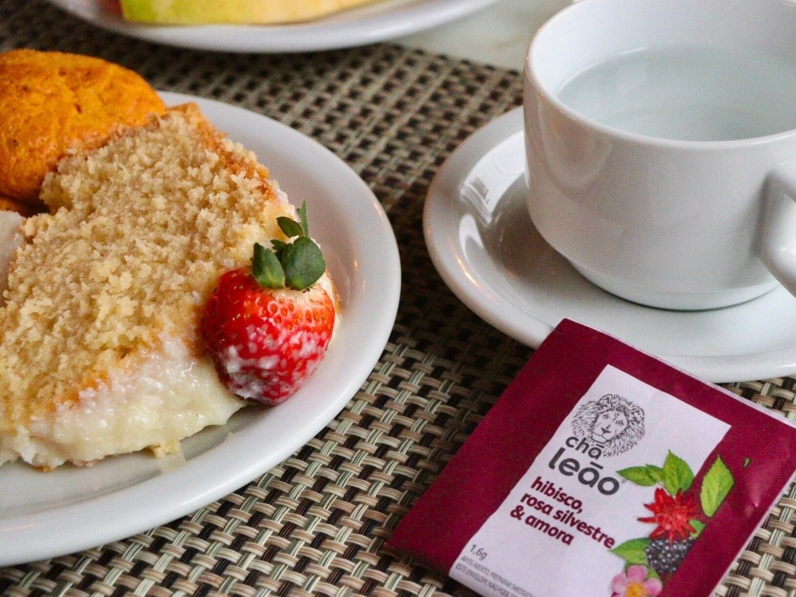 Un plato con un postre, una fresa y una taza de té sobre un mantel tejido.