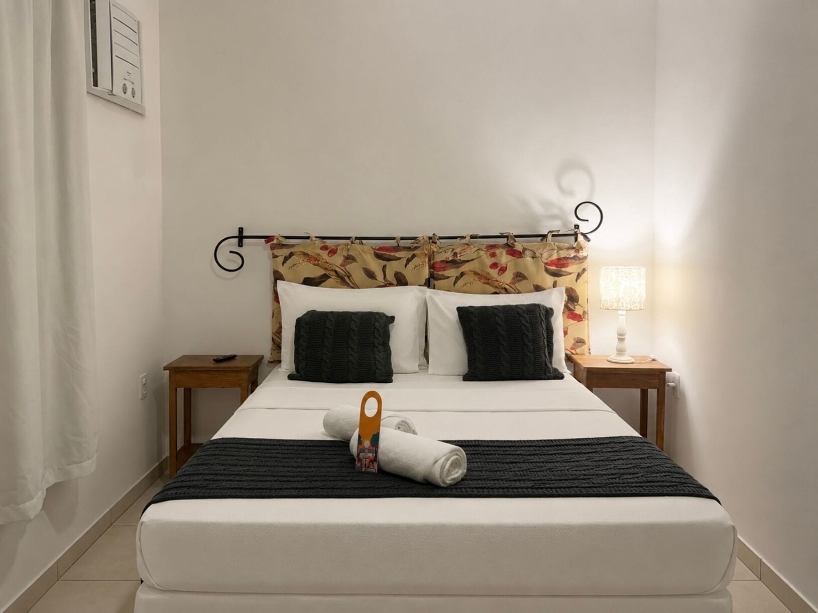 A neatly made bed with a black and white striped blanket, a pillow, and a rolled towel on the bed.