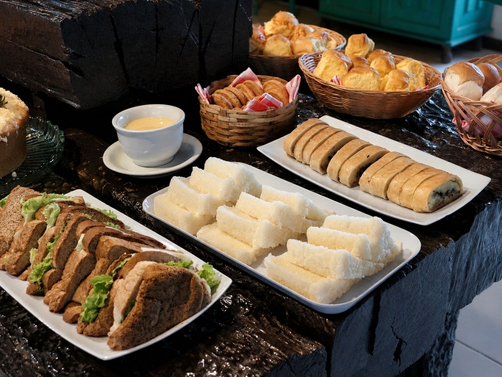 Une table de buffet proposant divers plats, notamment des sandwichs, des petits pains et des pâtisseries.