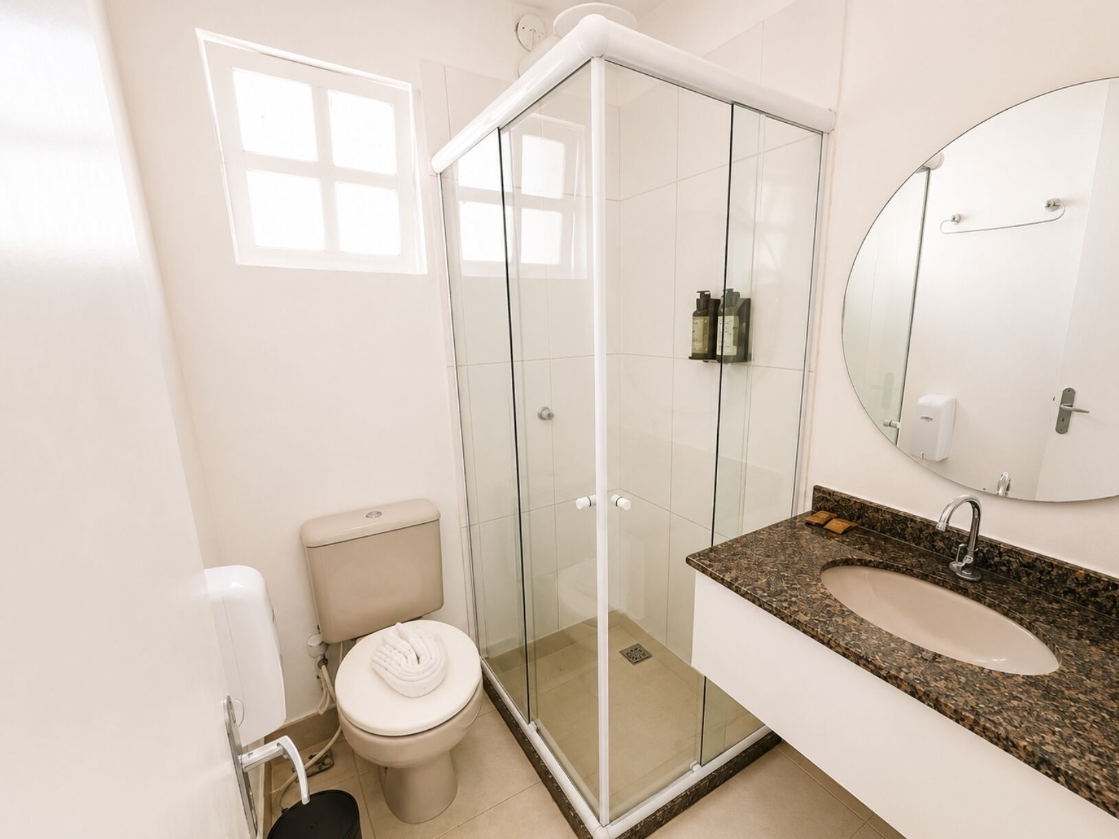 A modern bathroom with a glass-enclosed shower, a toilet, and a sink with a granite countertop.