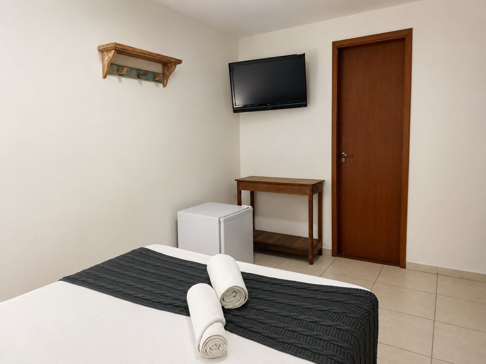 A hotel room with a bed, a television mounted on the wall, a wooden door, and a small table.