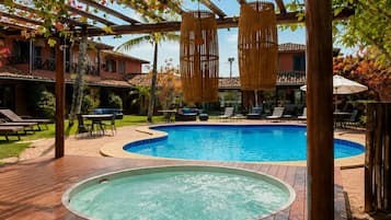 A pool area with a hot tub, lounge chairs, and a pergola with hanging lamps.