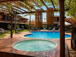 Un área de piscina con un jacuzzi, sillas de descanso y una pérgola con lámparas colgantes.