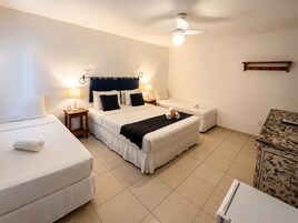 Habitación de hotel con una cama grande, dos camas más pequeñas, un ventilador de techo y una mesita de noche con lámparas.