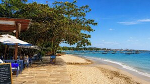 A coastal beachside restaurant with outdoor seating, a wooden pergola, and a view of the sea with boats. - Pousada Sable Dor (Búzios)