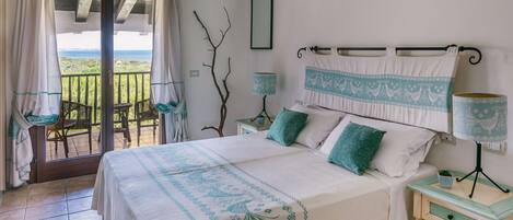 A bedroom with a bed, two bedside tables, a nightstand, a window with curtains, a view of the outdoors, and a wall-mounted mirror.