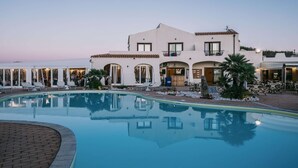 Un hôtel doté d’une piscine, d’un espace extérieur aménagé et d’un bâtiment blanc orné de balcons.
