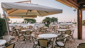Une terrasse extérieure avec des tables et des chaises en osier, des parasols et une piscine en arrière-plan.