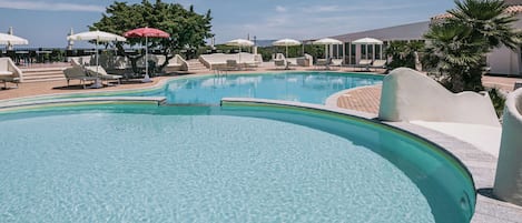Ein Poolbereich mit Liegestühlen und Sonnenschirmen, umgeben von Palmen und blauem Himmel.
