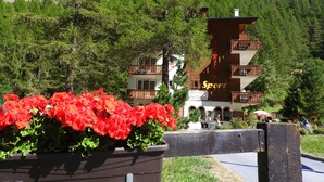 Un hotel con varios balcones, un cartel que indica que es un hotel deportivo y un telón de fondo montañoso.