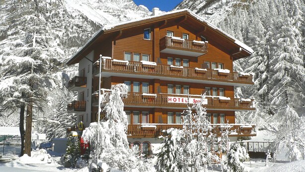 Un hotel de madera de varios pisos con balcones, rodeado de árboles y montañas cubiertas de nieve.