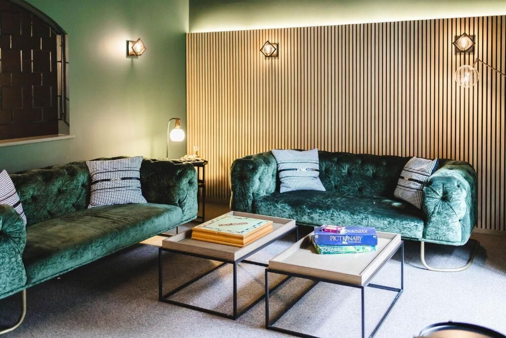 Um quarto com dois sofás de veludo verde, uma mesa de centro e uma parede com ripas de madeira vertical.