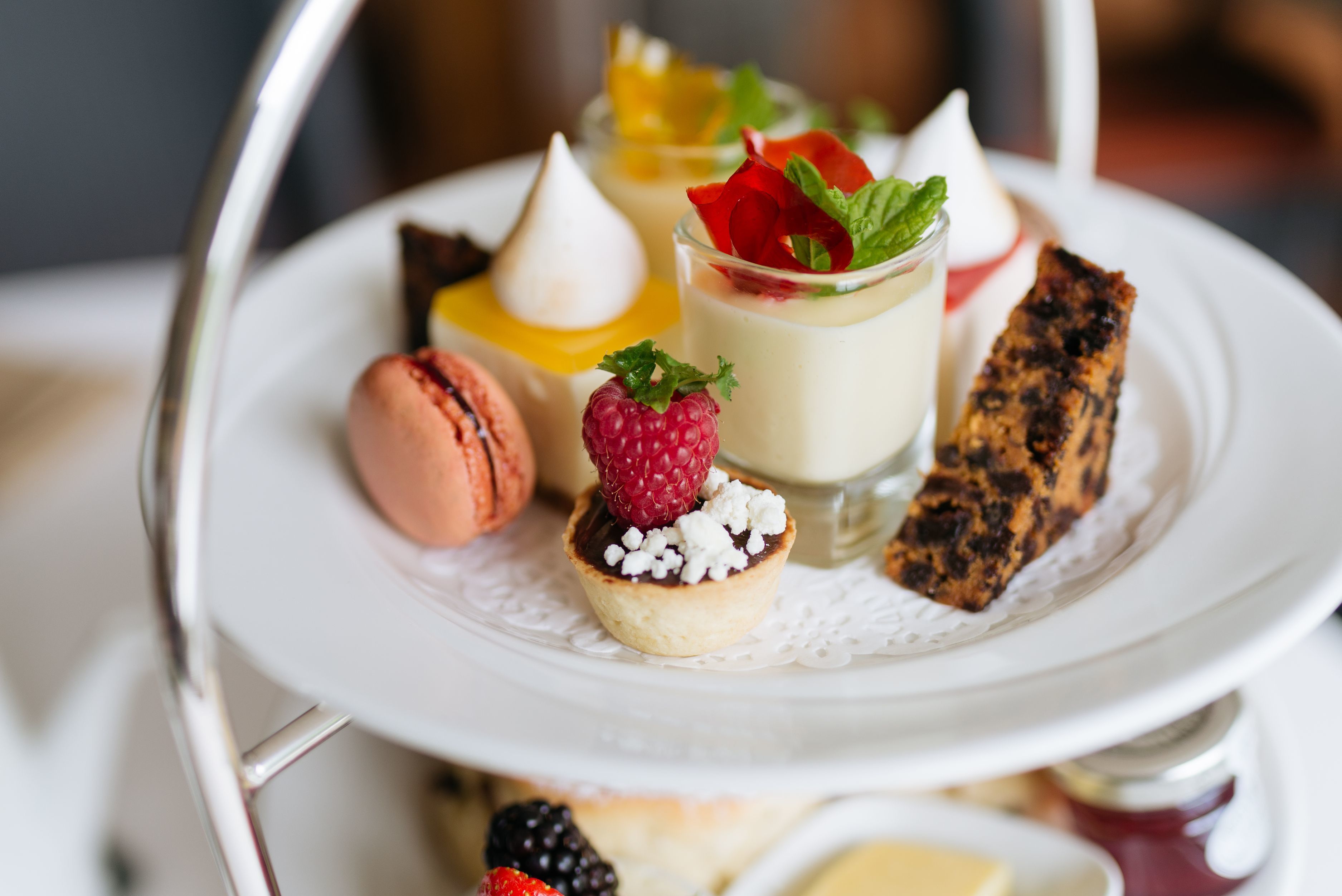 A tiered dessert tray with various pastries and a glass of a creamy beverage, possibly tea or coffee.