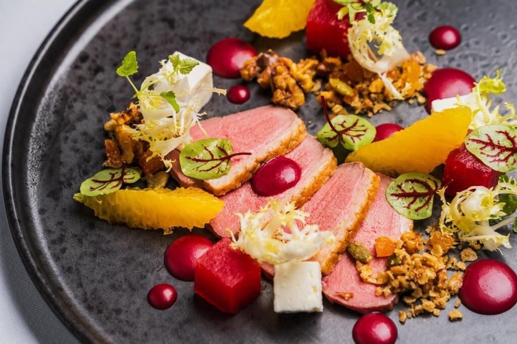 Une assiette de nourriture comprenant de la viande coupée en tranches, des fruits et des accompagnements.