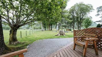 Un banco de madera en una terraza con vista a un área verde con árboles y una valla.
