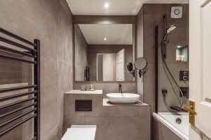 Un baño moderno con un espejo grande, un lavamanos redondo, una ducha y un perchero para toallas.