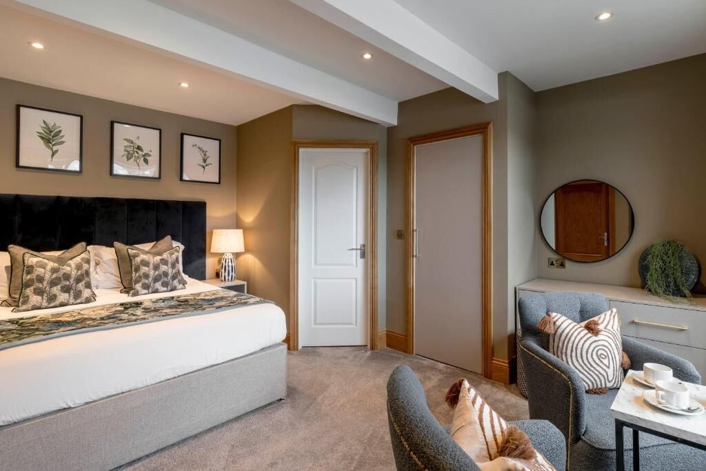 A bedroom with a bed, bedside table, lamp, and a wall with framed botanical prints.