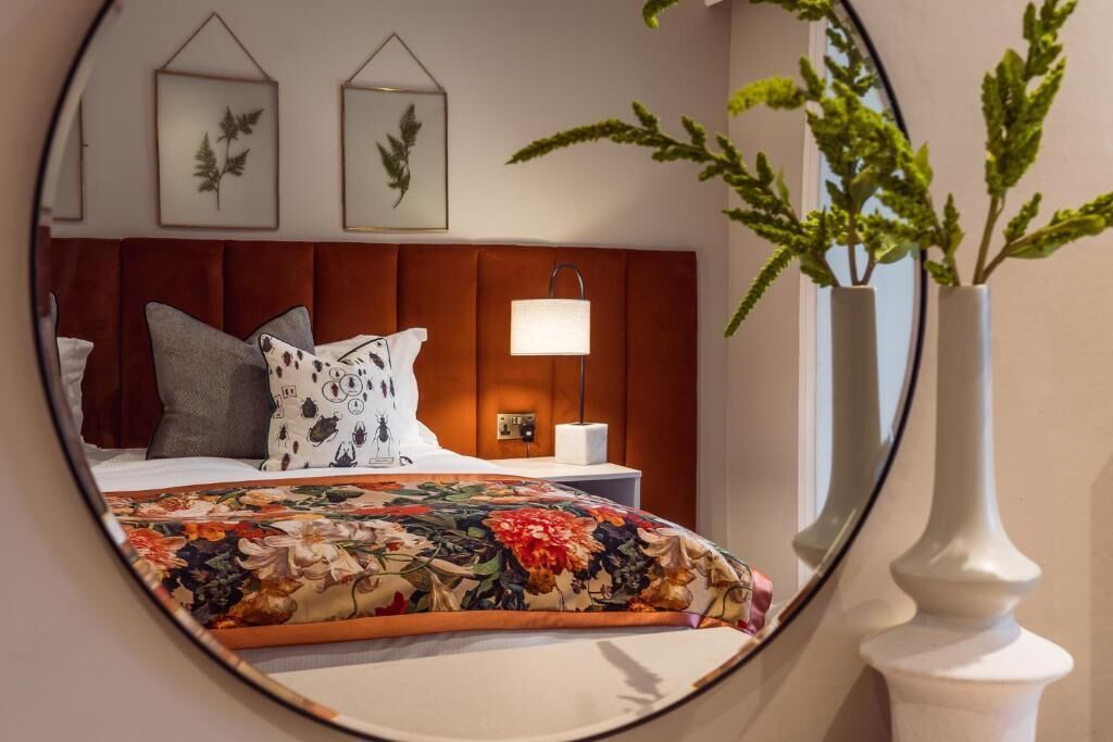 Habitación de hotel con cama, mesita de noche, lámpara, impresiones enmarcadas de motivos botánicos en la pared y una planta en maceta.