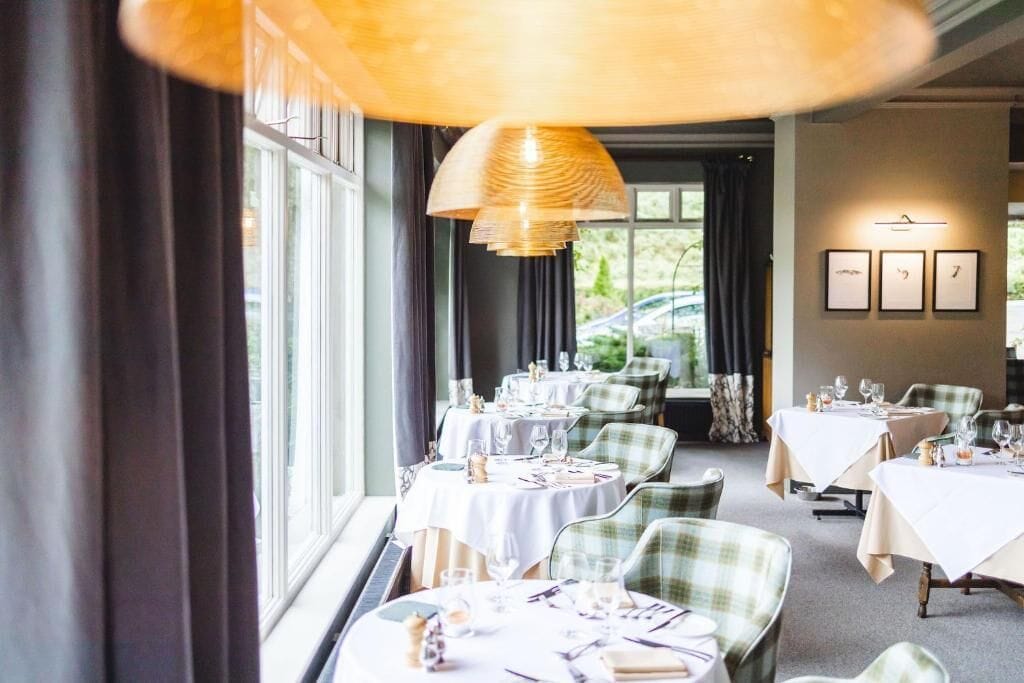 A restaurant with round tables, green plaid chairs, and a large hanging light fixture.