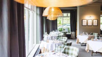 A restaurant with round tables, green plaid chairs, and a large hanging light fixture.