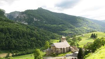 A stone building with a bell tower, surrounded by lush green hills and a valley.