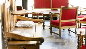 A seating area with wooden benches and red upholstered chairs, a backpack, and hiking boots on the floor. - Hôtel Etchémaïté (Larrau)