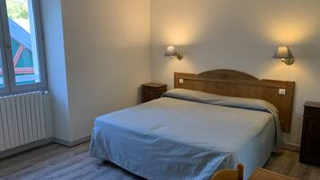 Een slaapkamer met een bed, twee nachtkastjes, een houten hoofdbord, een raam en een radiator.