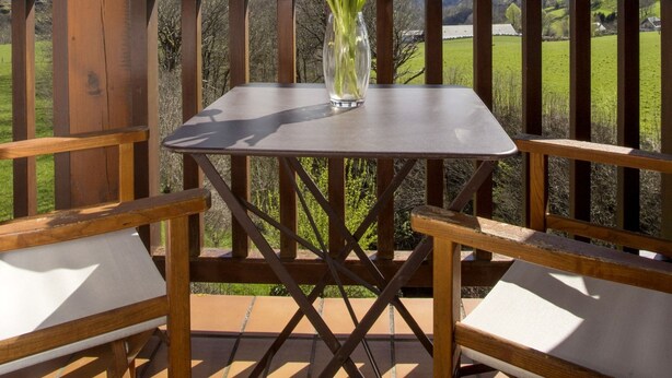 A wooden deck with a table and chairs, a vase with flowers, and a scenic mountain view. - Hôtel Etchémaïté (Larrau)