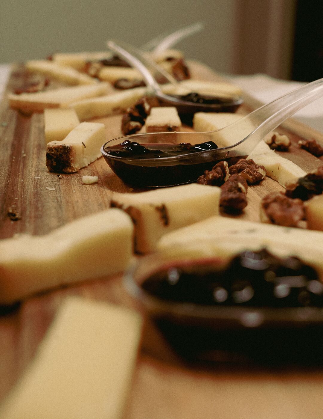 A wooden board with various cheeses and nuts, accompanied by a small bowl of dark jam.