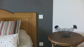 Un dormitorio con cabecera de madera, almohadas a rayas, una silla de mimbre y un interruptor de pared.
