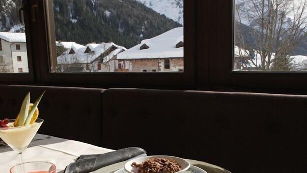 Un tavolo con vista sulle montagne innevate attraverso una finestra, un piatto di dessert, una tazza di caffè e pasticcini.