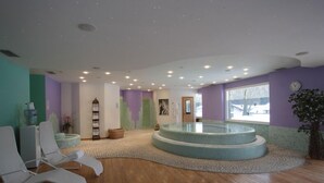 Una stanza spa con una vasca idromassaggio circolare, pavimento in legno e vista sull'esterno tramite un'ampia finestra.