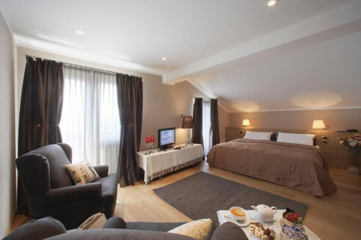 Hotelkamer met een bed, een bureau met computer, een stoel en een bijzettafeltje met ontbijtartikelen.
