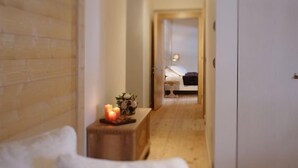 Un corridoio stretto con pavimento in legno che conduce a una camera da letto con un letto e un comodino con candele.